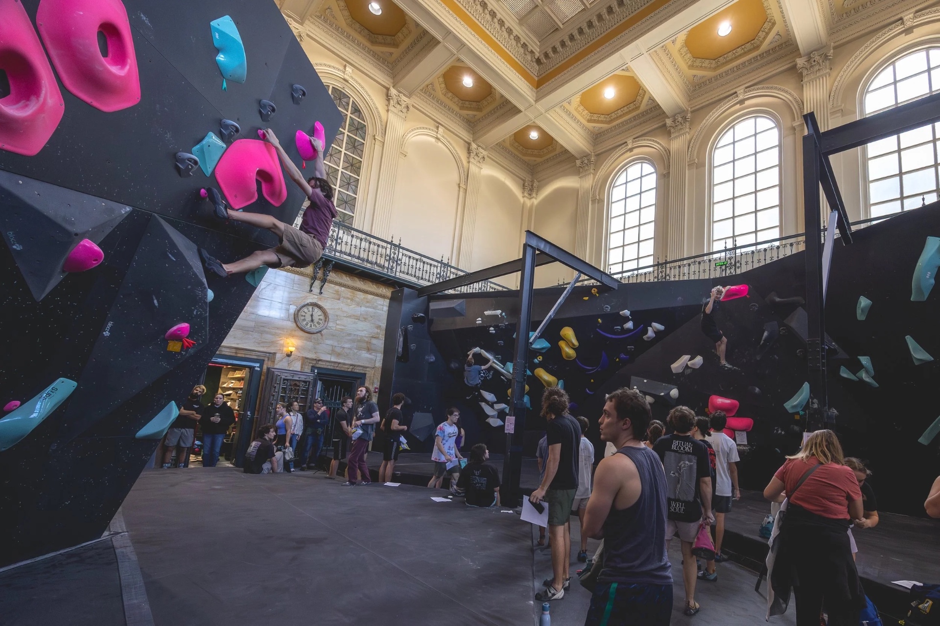 Boulder Union's grand climbing hall inside the historic former New Bedford Institution for Savings, with climbers on colorful boulders beneath coffered ceilings and arched windows
